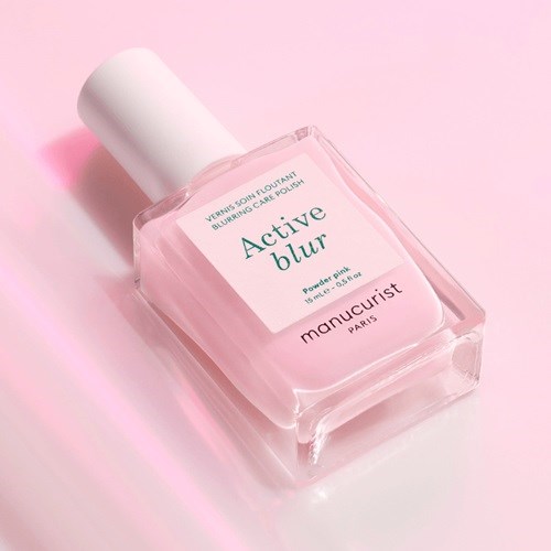 En glassflaske med neglelakk merket Active Blur i rosa og hvitt, på en rosa bakgrunn.