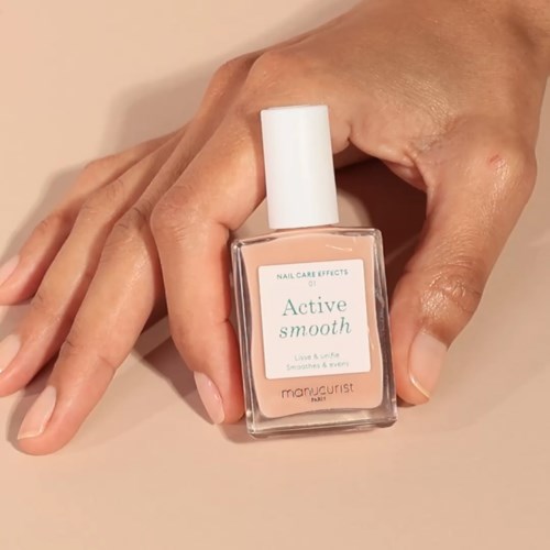 A hand holding a bottle of nail polish labeled 'Active Smooth' near a light-colored surface.