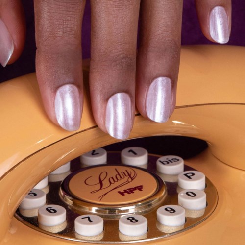 Eine Hand mit metallischen Nägeln liegt auf einem Vintage-Telefon mit der Aufschrift Lady. Die einzelnen Ringzahlen umgeben die zentrale Wählscheibe.