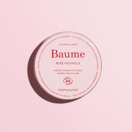 Round container of organic universal balm with pink label and red text, on a light pink background.