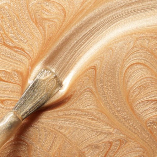 A paintbrush spreads light beige paint on a surface, creating swirling patterns and textures.
