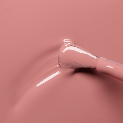 A pink makeup brush is pressed into a smooth pink surface, making a small dent.
