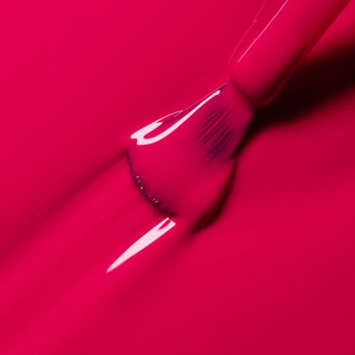 A makeup brush smudges bright pink lipstick on a pink background.
