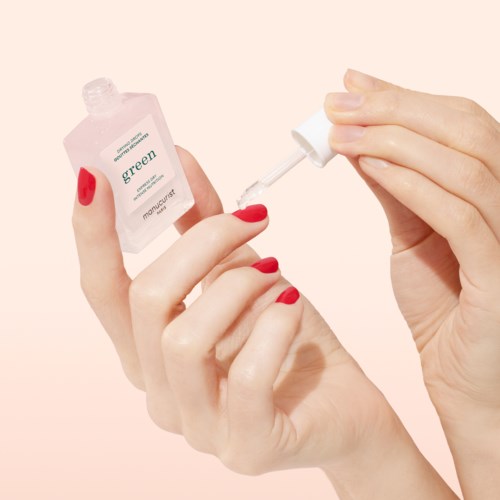 A person with red nail polish is applying green nail polish with a brush. The background is light pink.