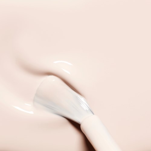 A facial brush applies creamy white skincare product to skin.