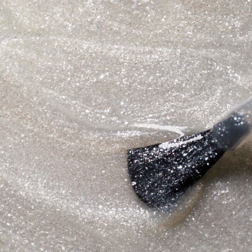 A makeup brush is spreading glittery silver powder on a surface.