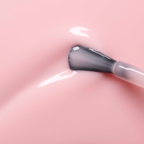 A makeup brush is applying white cream to pink skin.