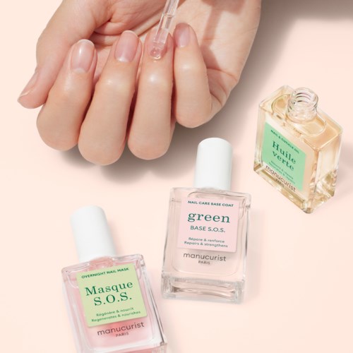 En person använder en dropper för att applicera klart nagelolja, med tre flaskor nagelprodukter i närheten på en ljus yta.