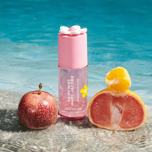 Maracuja geurstmist met roze deksel, naast een appel en half grapefruit, op zandgrond bij water.