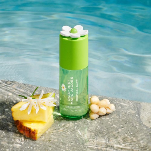 Een groene sprayfles met een witte madeliefje dop, op een steen naast ananas en witte stenen bij water.