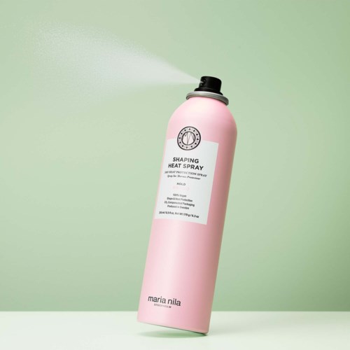 En rosa flaska med värmeskyddsspray och svart munstycke mot en grön bakgrund.