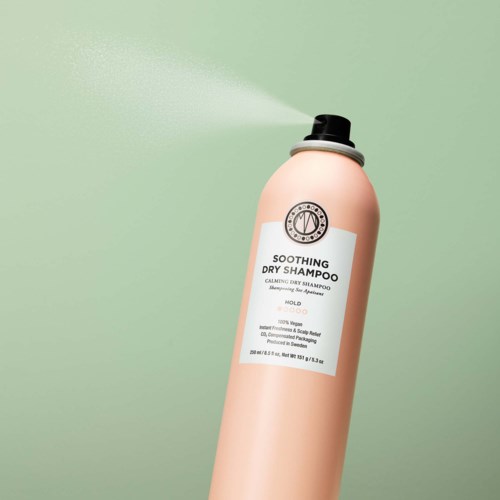 Eine rosa Flasche sprüht Trockenshampoo vor einem hellgrünen Hintergrund. Sie hat einen schwarzen Deckel und ein weißes Etikett.