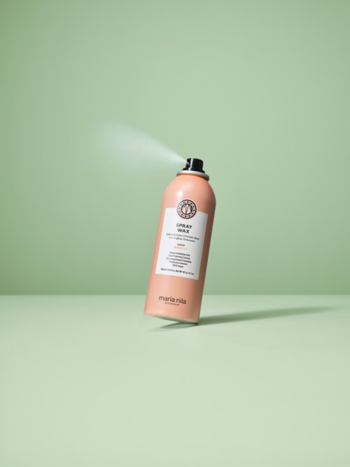 En rosa sprayflaska märkt 'Spray Wax' lutar i en vinkel och sprayar ut dimma mot en grön bakgrund.