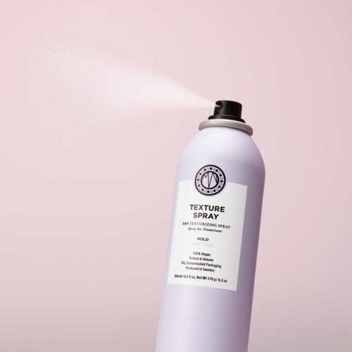 A white spray can sprays out a fine mist against a light pink background.
