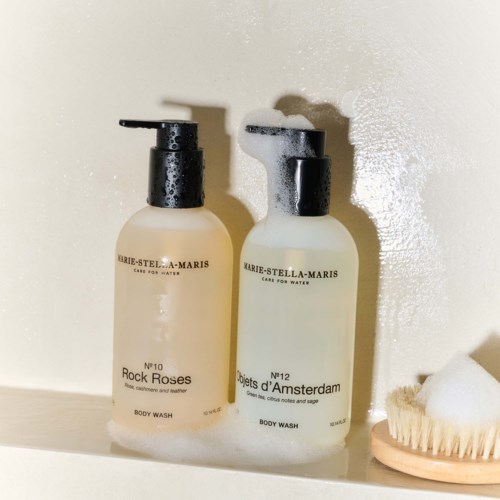 Two white bottles of body wash stand side by side, one with foam on top, next to a brush and sponge.