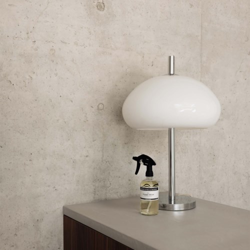 En vit lampa och en sprayflaska står på en grå yta mot en vägg med textur.