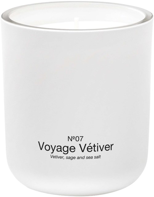 Et hvidt stearinlys i en enkel beholder med mærket Voyage Vétiver. Den nævner salvie og havsalt.