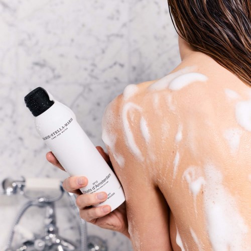 En person vasker skulderen med sæbe og shampoo, og skummer huden i et badrum.