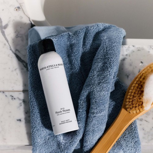 Et bad med et håndklæde, shampoo-flaske og en børste med sæbe på en marmoroverflade.