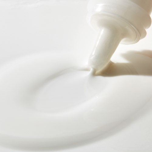 A white squeeze bottle dispenses cream or lotion onto a smooth surface.