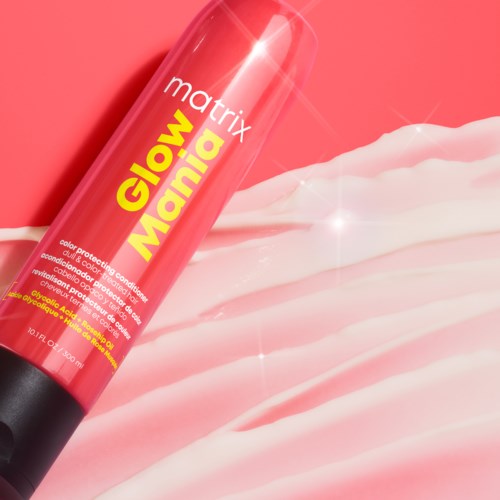 En röd sprayflaska märkt 'Glow Mania' med lite kräm eller lotion runt den, på en rosa yta.
