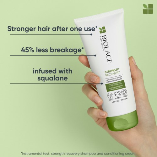 En hand håller ett rör med Biolage Strength Recovery schampo, med nyckelfördelar listade på en ljusgrön bakgrund.