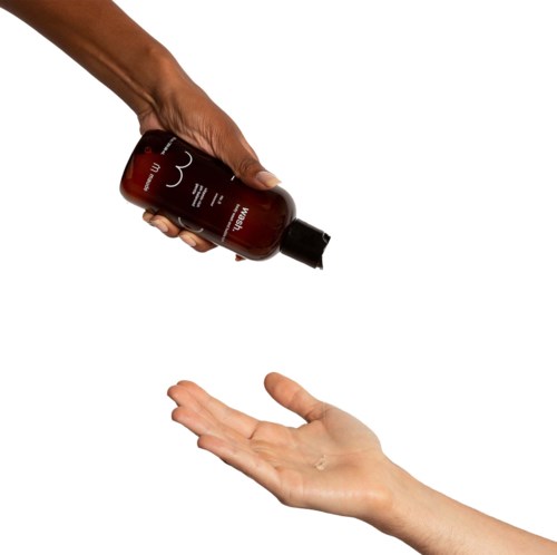 A person pours lotion or soap from a bottle onto their palm in a simple, clean setting.
