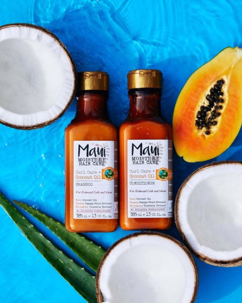 Två små flaskor med Maui hårvårdsprodukter omgivna av kokosnötter, papaya och aloe Vera på en blå bakgrund.