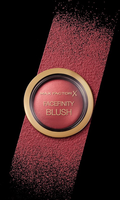 Ett runt blushbege med guldkant, rosa blushpulver sprids på svart bakgrund. Etiketten säger "Facefinity Blush."