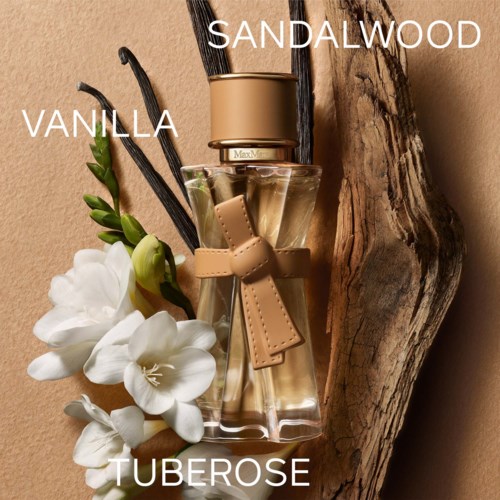 En parfame uden med dufte af vanilje, sandeltræ og tuberose, pyntet med en sløjfe, ved siden af blomster og træ.