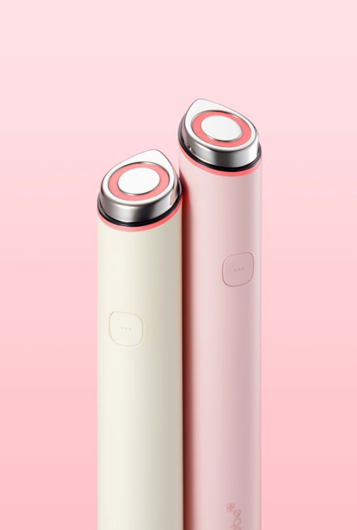 Två eleganta, cylindriska enheter i creme och rosa färger med rundade toppknappar, mot en rosa bakgrund.