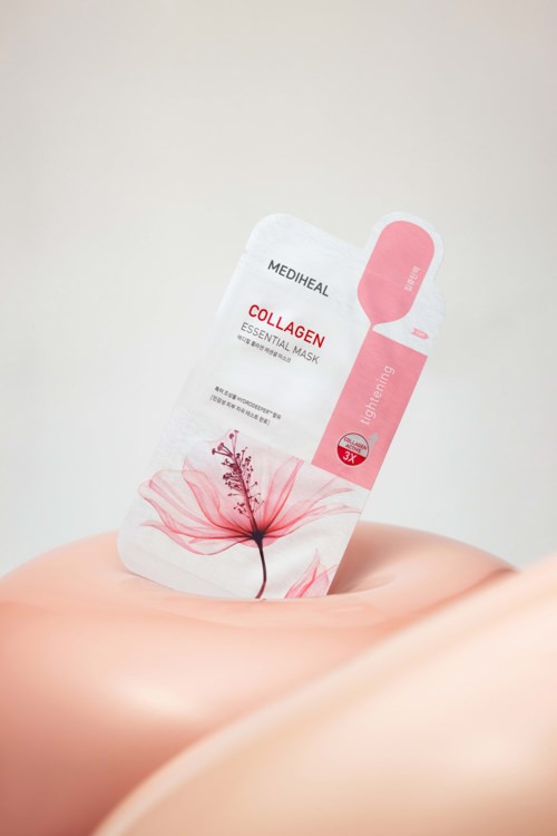 Ett hudvårdsmaske paket med rosa blommor och text, hålls i en persons hand mot en vit bakgrund.