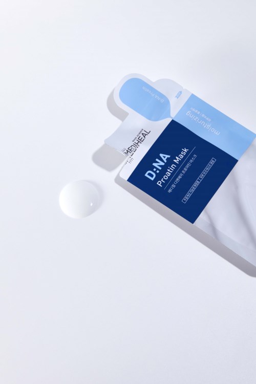 En boks DNA-probiotikamaske med en liten klatt krem ved siden av på en hvit overflate.