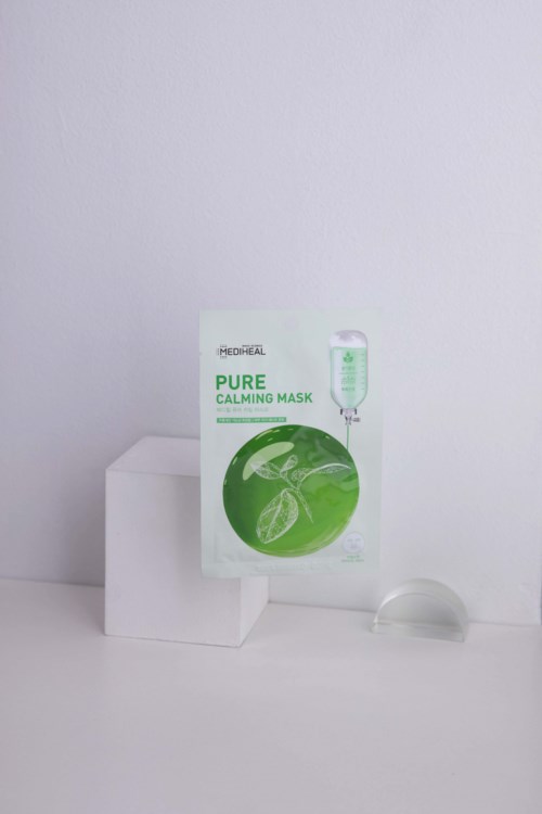 A face mask product box with green and white color, placed on a white surface with minimal background.