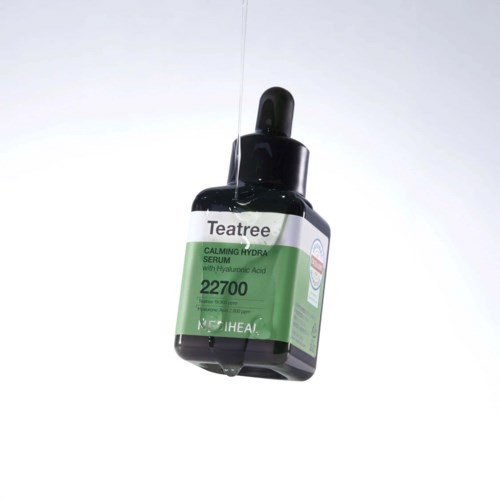 En dråpetinne over en svart flaske med Teatree beroligende serum med hyaluronsyre, etiketten inneholder produktdetaljer.