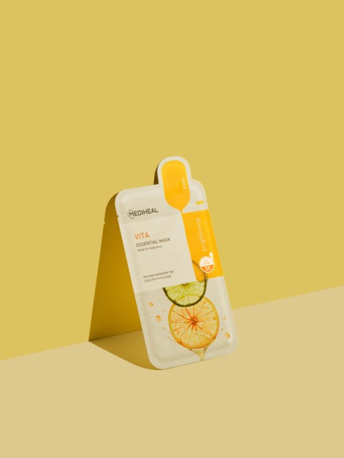 Et hudpleieprodukt i en flat pose med appelsin- og sitronskiver på, merket 'VITA Essential Mask' mot en gul bakgrunn.