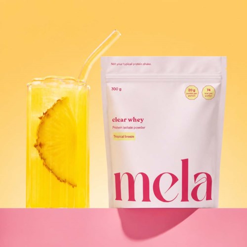 Hintergrund in Pink und Gelb mit einem Glas Ananas-Zitronen-Infusion neben einem weißen Beutel Proteinpulver.