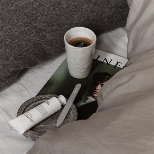 En kopp kaffe, en tidskrift med ett foto av en person, ett krämbelopp, och en sked på en säng.