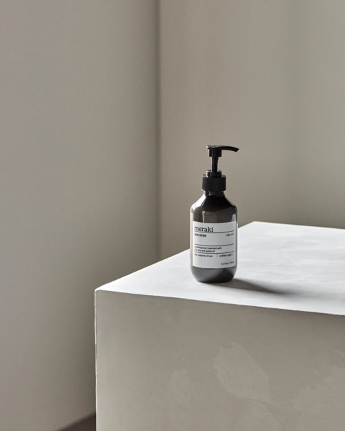 A black bottle with a pump sits on a white surface near a corner, against a plain wall.