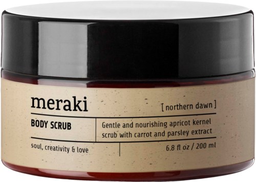 A jar of body scrub labeled 'meraki' with apricot kernel, carrot, and parsley extract. Black lid and beige container.