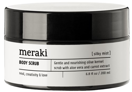 En hvit krukke med svart lokk med Meraki kroppsskrubb, merket som nærende med oliven, aloe og gulrot ekstrakt.