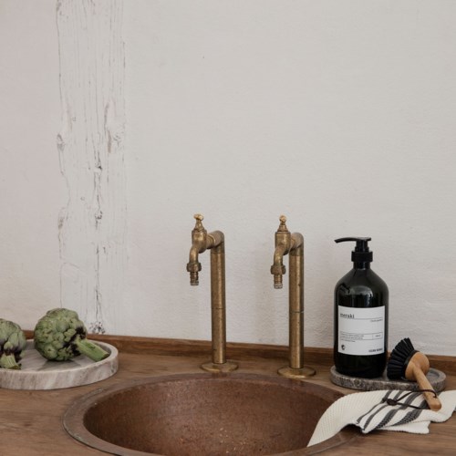 Zwei Vintage-Messinghähne, eine schwarze Seifenspenderflasche und Artischocken auf einem Holztablett.