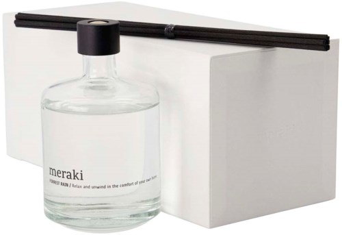En tydlig glasdoftdiffuserflaska med svarta stavar, vit låda och svart lock. Produktnamnet är 'meraki'.