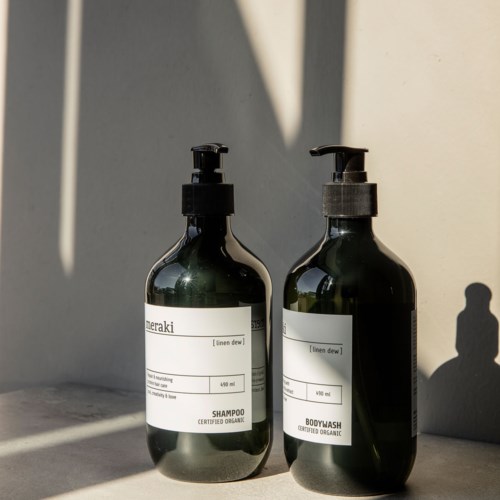 Two dark green bottles with pump dispensers, labeled for shampoo and body wash, sit on a surface with shadows.