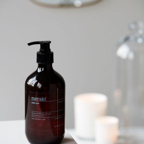 En mörkbrun handtvålshållare med pump, placerad på en ljus yta med ljus och en glaskärl i närheten.