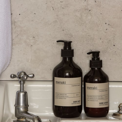 Två mörka flaskor med handtvål och lotion står på en handfat med en beige vägg som bakgrund.
