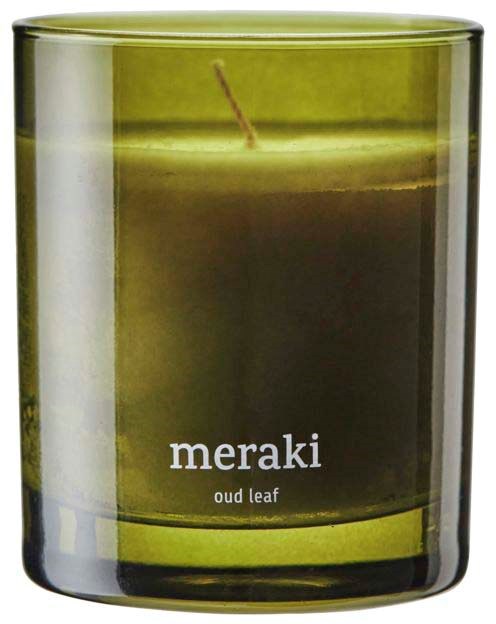 Et grønt duftlys i et glas, mærket 'meraki oud leaf'.