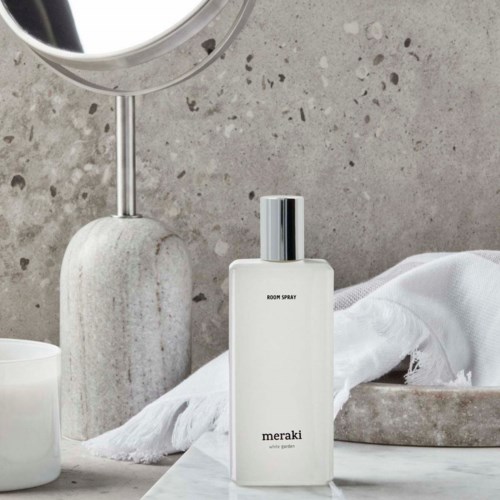A white spray bottle on a bathroom counter, with a mirror and gray textured wall in the background.