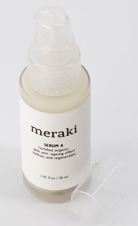 En vit flaska märkt "meraki" med pump, troligen en hudvårdsserum, med ett tydligt lock bredvid.