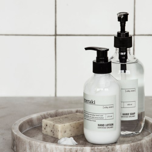 To flasker med håndsåpe og lotion, en såpe og et lite håndkle på et brett i et bad.